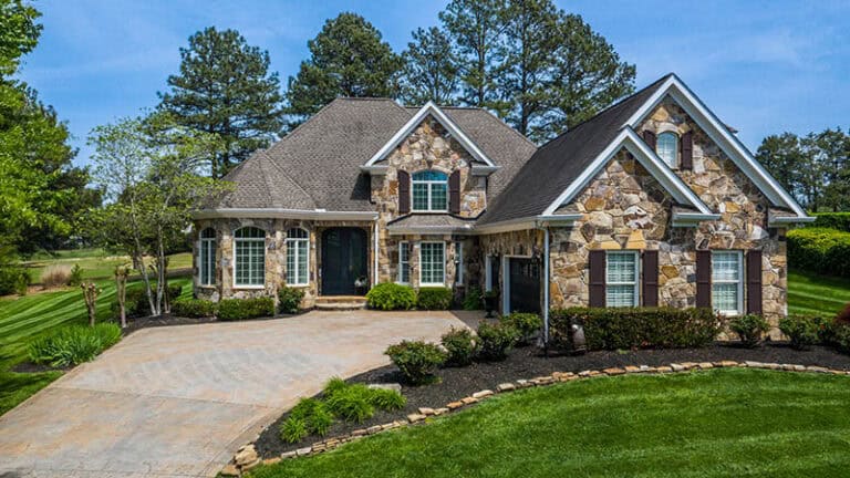 High-quality stone home with landscaped yard and paved driveway, showcasing upscale architecture.